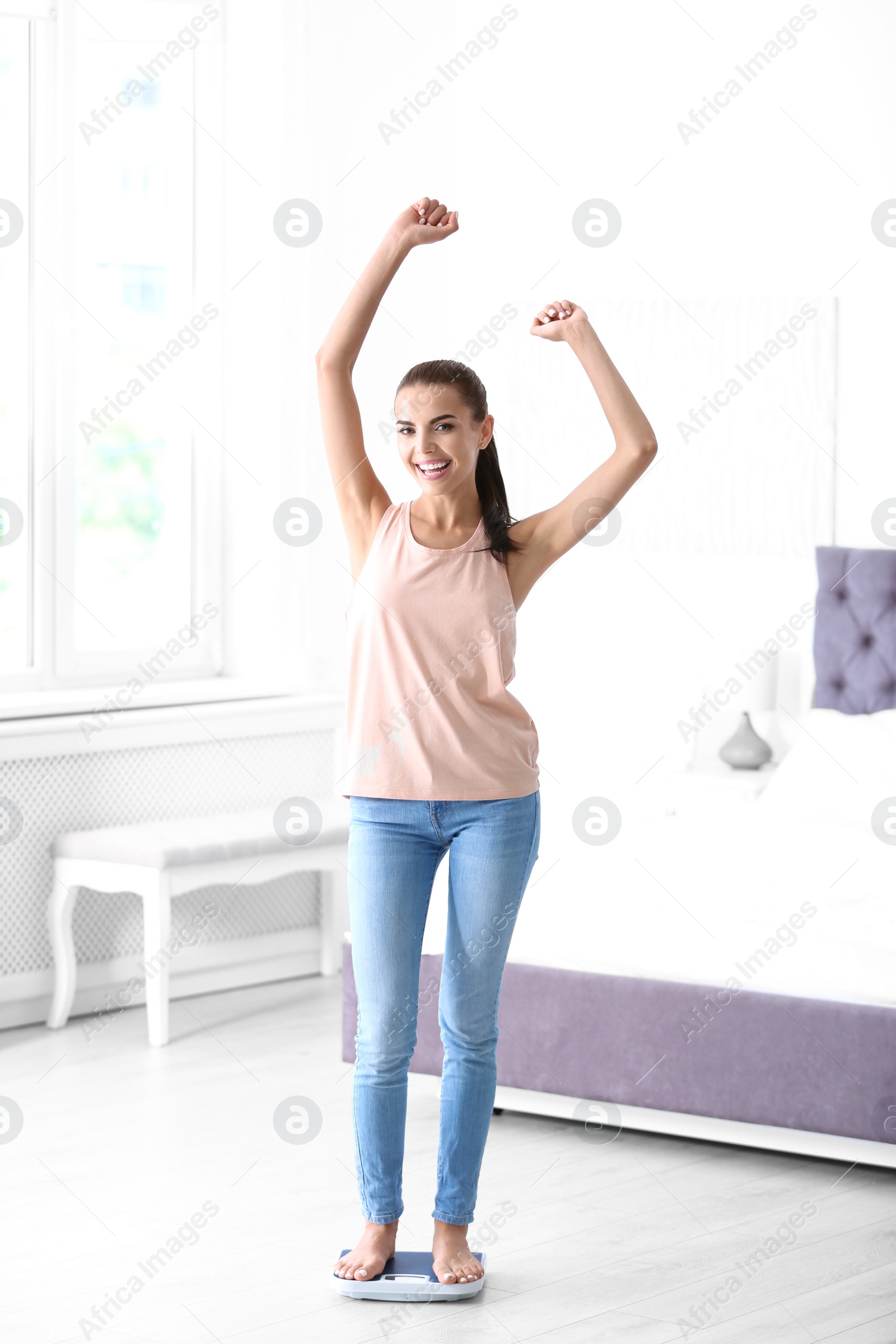 Photo of Happy young woman measuring her weight using scales at home. Weight loss motivation