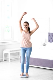 Happy young woman measuring her weight using scales at home. Weight loss motivation