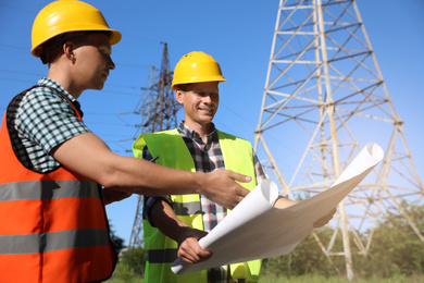Professional electricians with drafting near high voltage tower