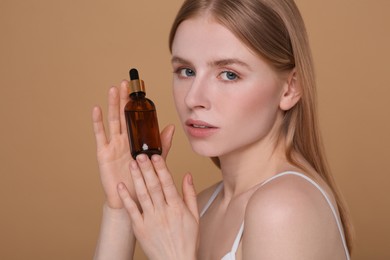 Photo of Beautiful young woman with bottle of essential oil on brown background