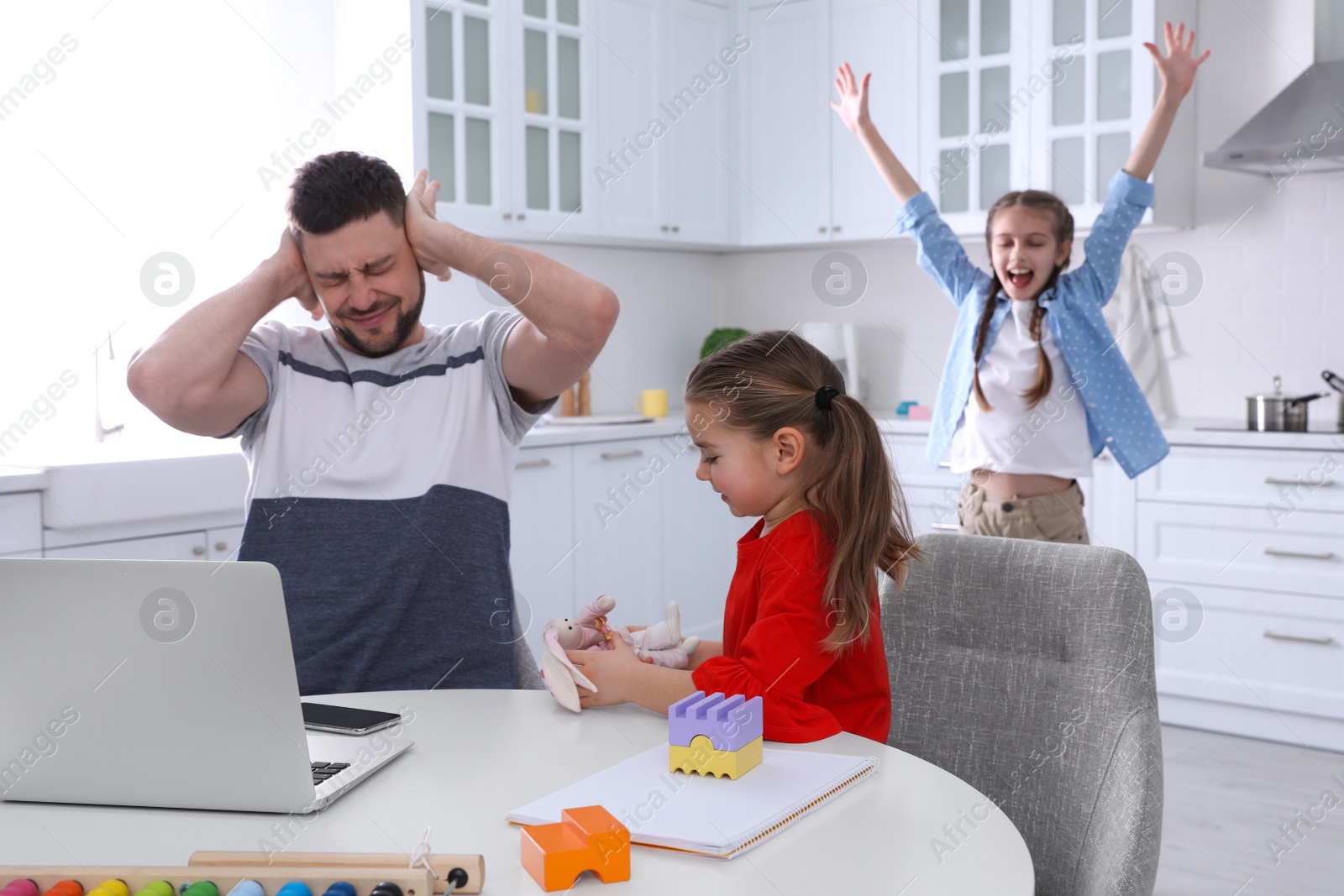 Photo of Children disturbing stressed man in kitchen. Working from home during quarantine