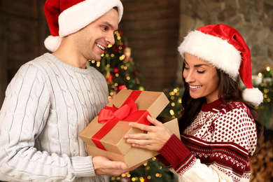 Photo of Happy couple with gift box in living room decorated for Christmas