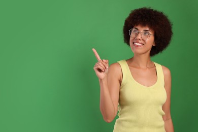 Photo of Happy young woman in eyeglasses pointing at something on green background. Space for text