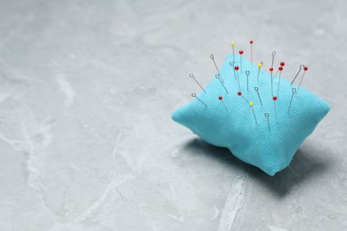Photo of Light blue pincushion with sewing pins on grey table. Space for text