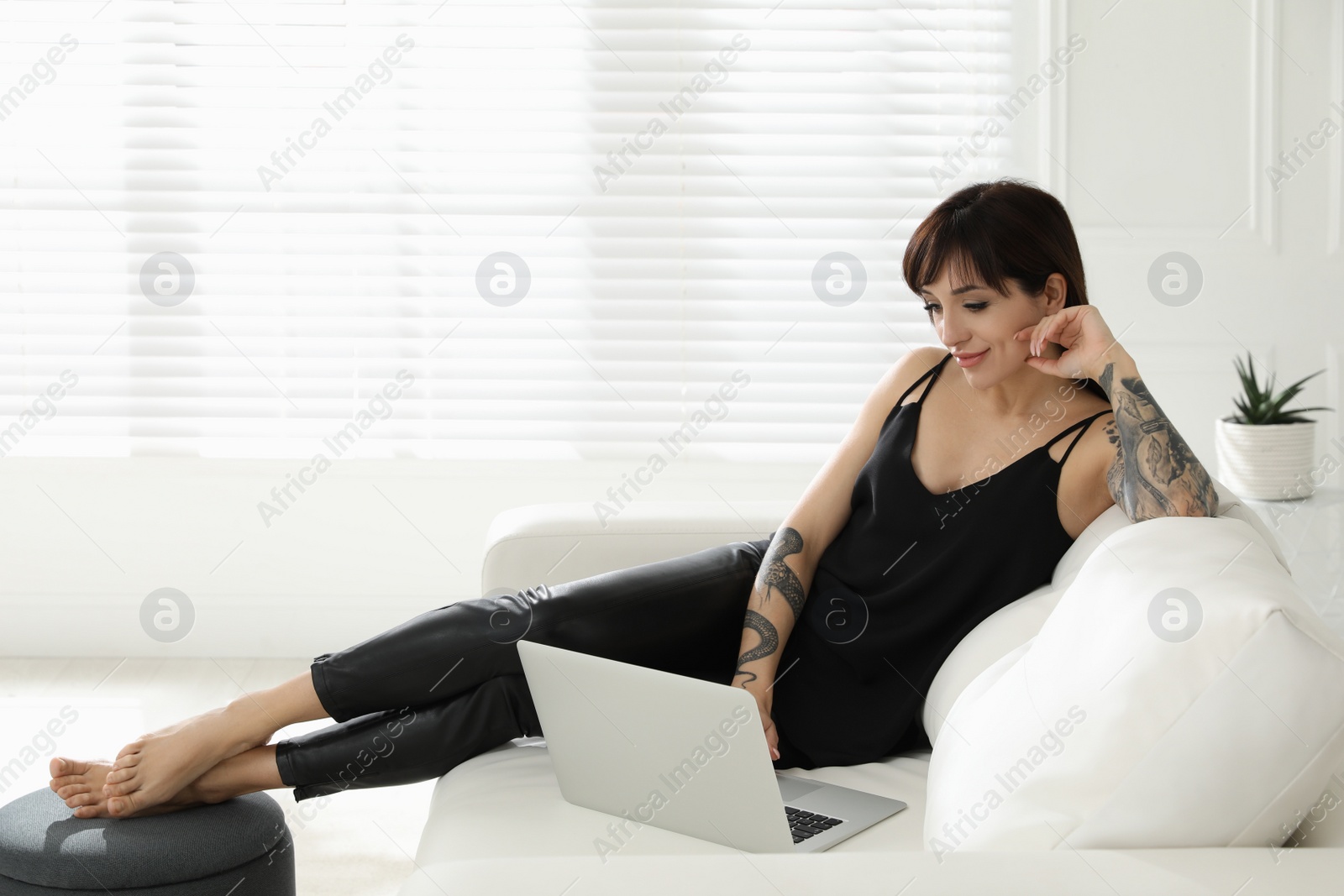 Photo of Beautiful woman with tattoos on arms using laptop in living room