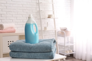 Photo of Bottle of detergent and clean towels on table indoors, space for text. Laundry day