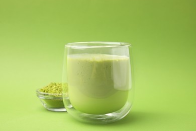 Glass of tasty matcha smoothie and powder on green background, closeup