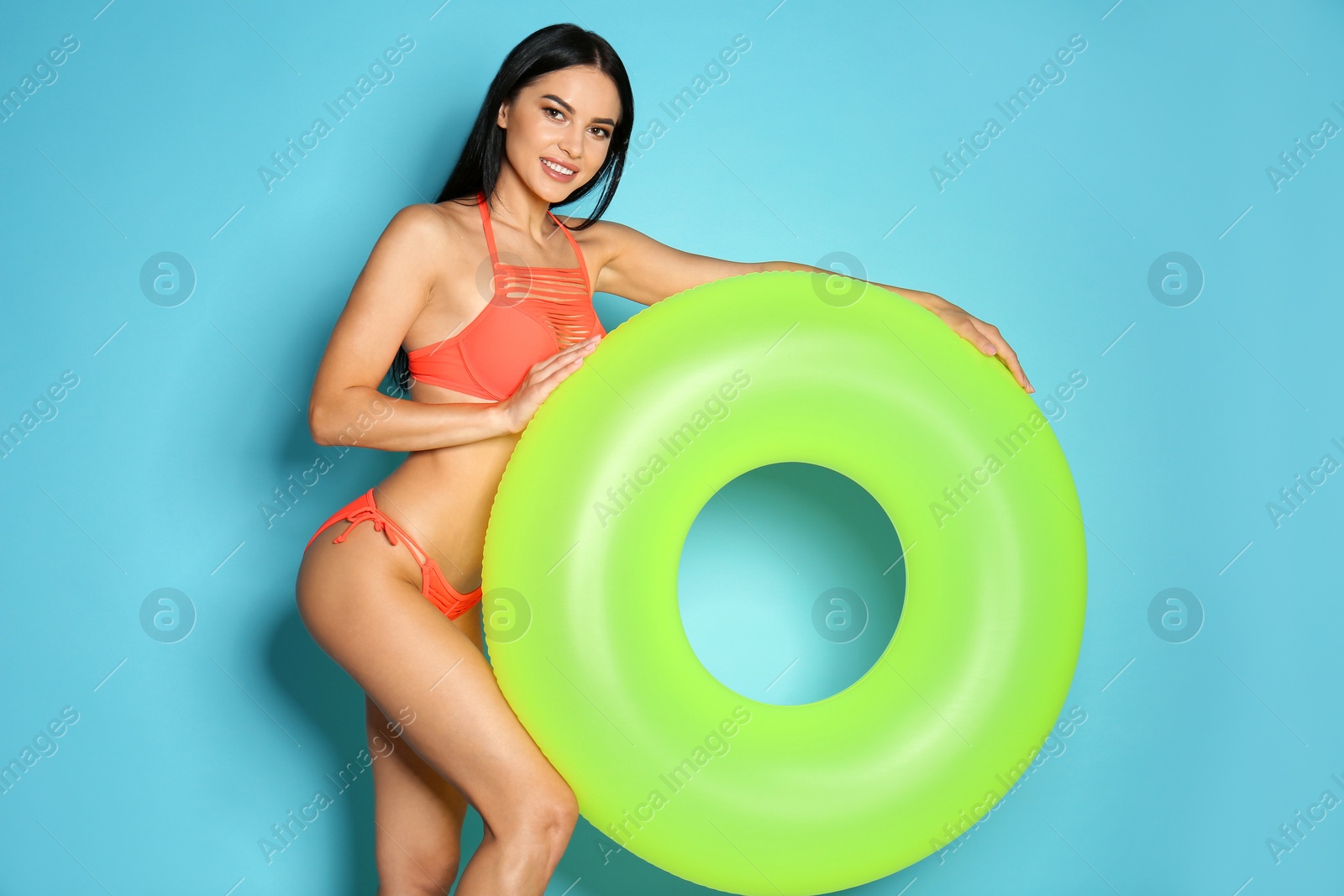 Photo of Beautiful young woman in stylish bikini with green inflatable ring on light blue background