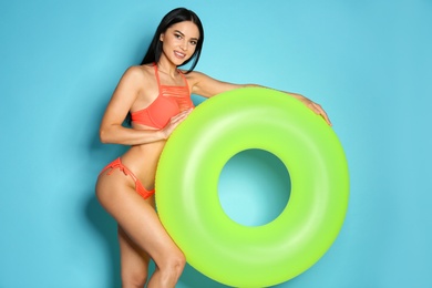 Photo of Beautiful young woman in stylish bikini with green inflatable ring on light blue background