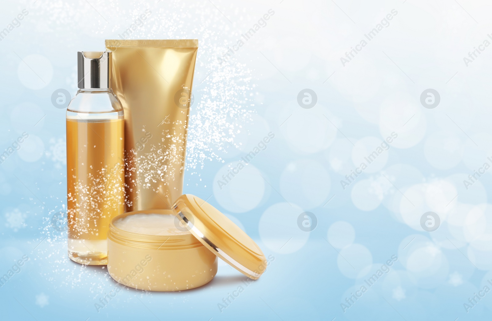 Image of Different cosmetic products on light blue background with blurred snowflakes, space for text. Winter skin care