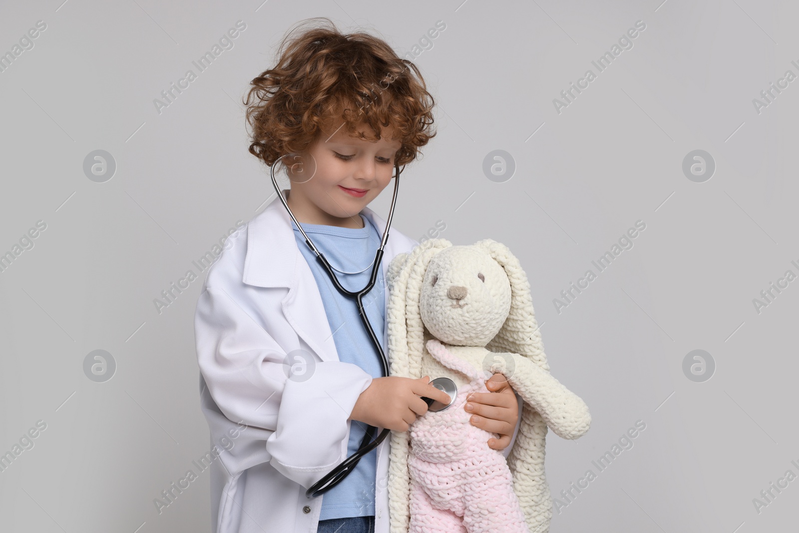 Photo of Little boy playing doctor with toy bunny on light grey background