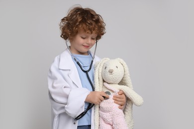 Photo of Little boy playing doctor with toy bunny on light grey background