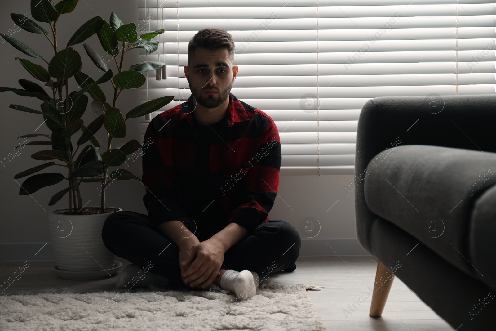 Photo of Sad man sitting near closed blinds indoors