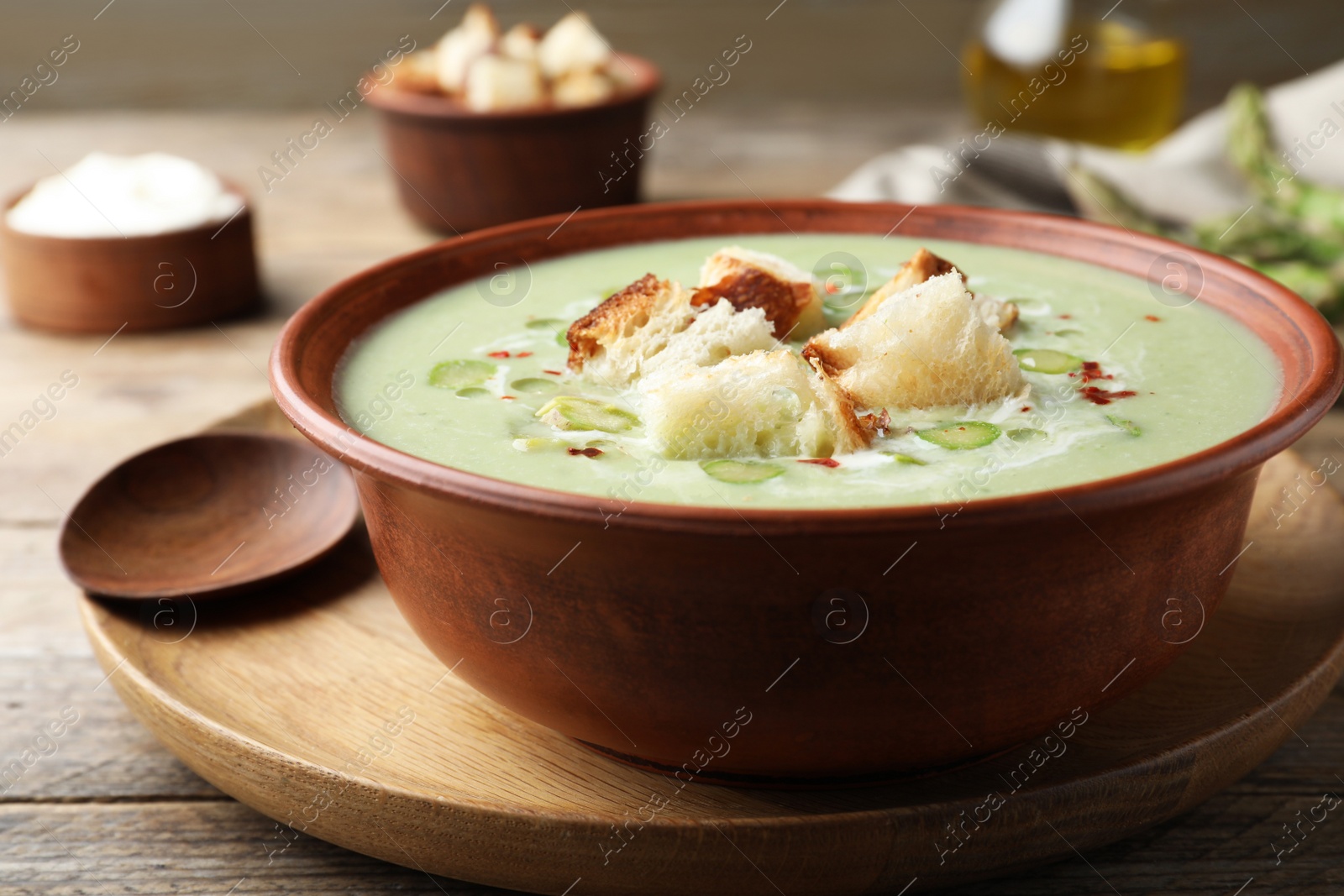 Photo of Delicious asparagus soup with croutons served on wooden table, closeup