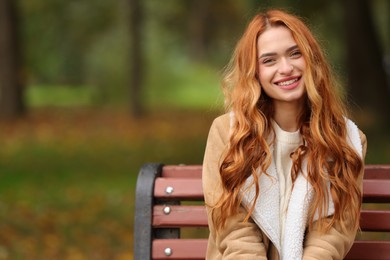 Portrait of smiling woman sitting on bench in autumn park. Space for text
