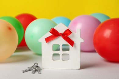 Photo of House model with red bow, keys and colorful balloons on white table. Housewarming party