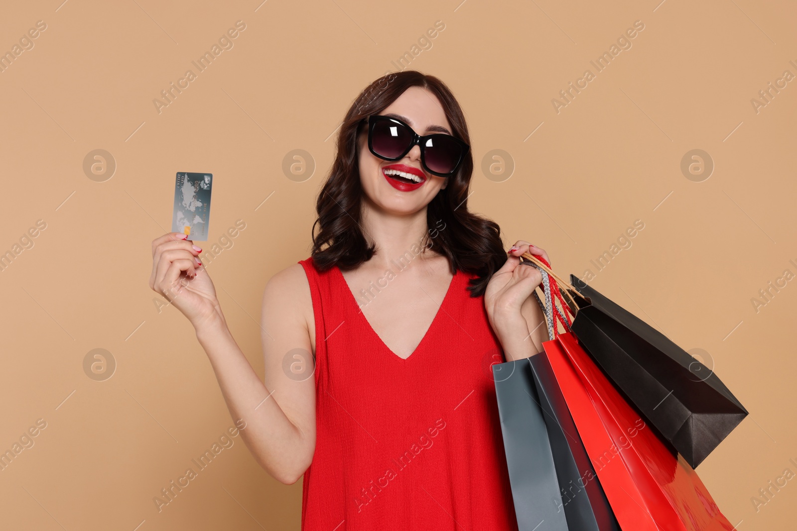 Photo of Beautiful young woman with paper shopping bags and credit card on beige background