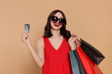 Beautiful young woman with paper shopping bags and credit card on beige background