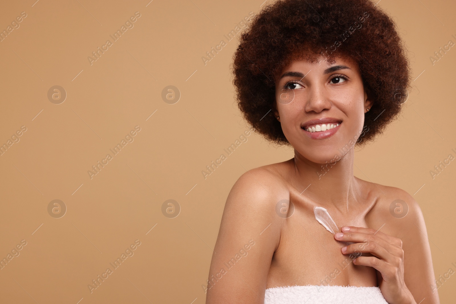 Photo of Beautiful young woman applying cream onto body on beige background, space for text