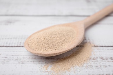 Spoon with granulated yeast on white wooden table, closeup