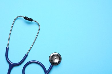 Stethoscope on light blue background, top view. Space for text