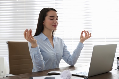 Photo of Businesswoman meditating at workplace in office. Stress relieving exercise