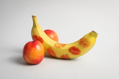 Photo of Banana with red lipstick marks and nectarines symbolizing male genitals on light grey background. Potency concept