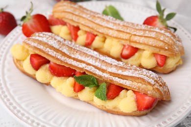 Delicious eclairs filled with cream, strawberries and mint on table, closeup