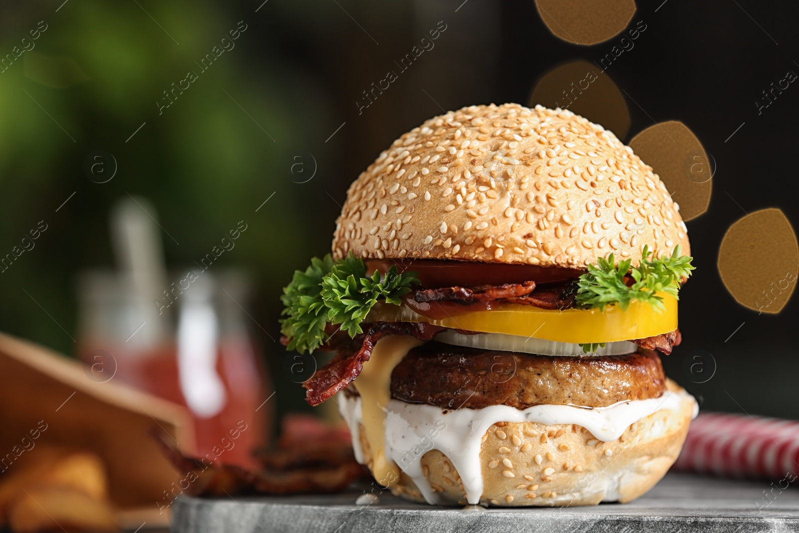 Photo of Fresh juicy bacon burger on board against blurred background. Space for text