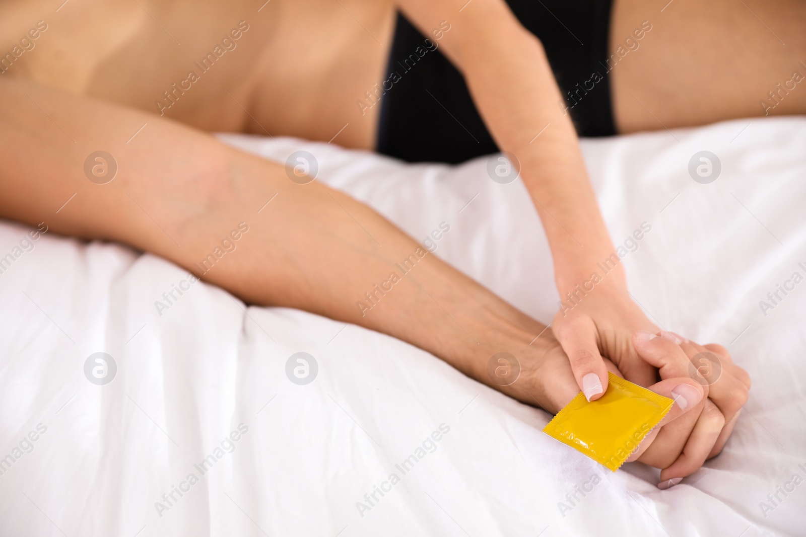 Photo of Woman and man holding condom together on bed, closeup. Safe sex concept