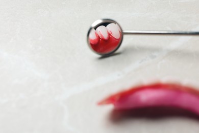 Photo of Dental mirror near gum model with blood on light grey table, closeup. Space for text