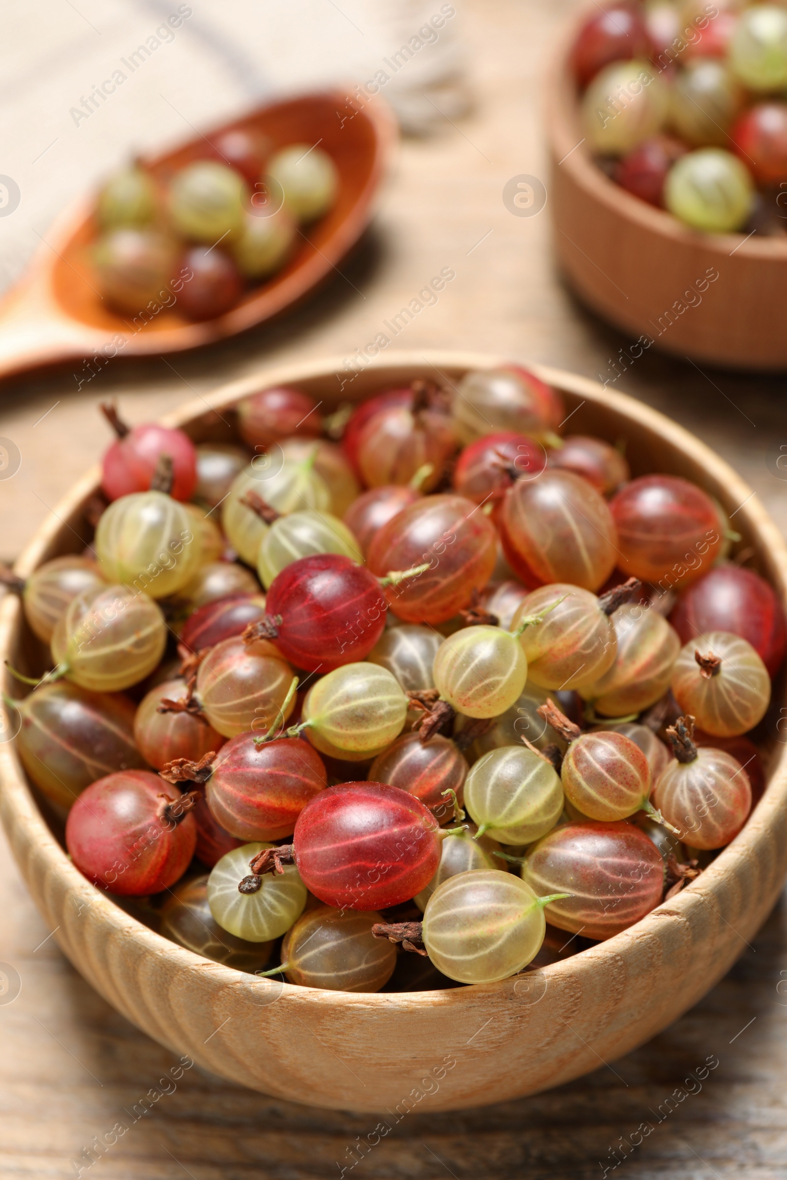 Photo of Bowl of fresh ripe gooseberries on wooden table, closeup