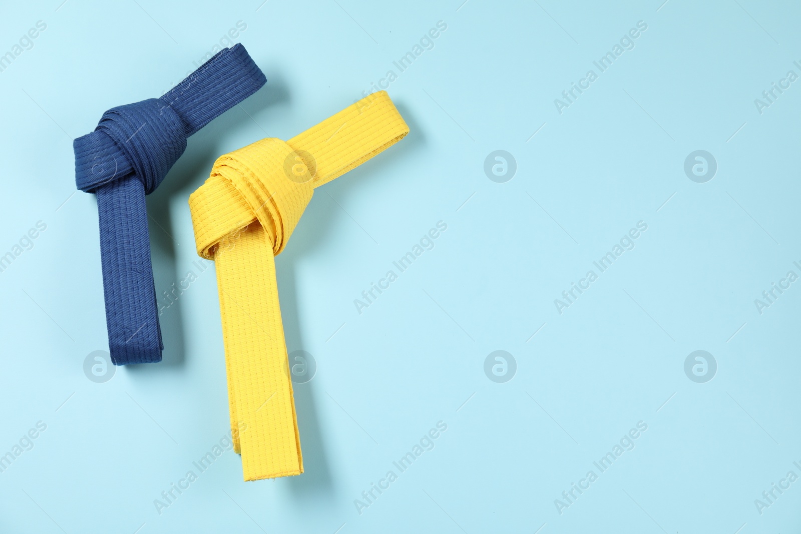 Photo of Colorful karate belts on light blue background, flat lay. Space for text