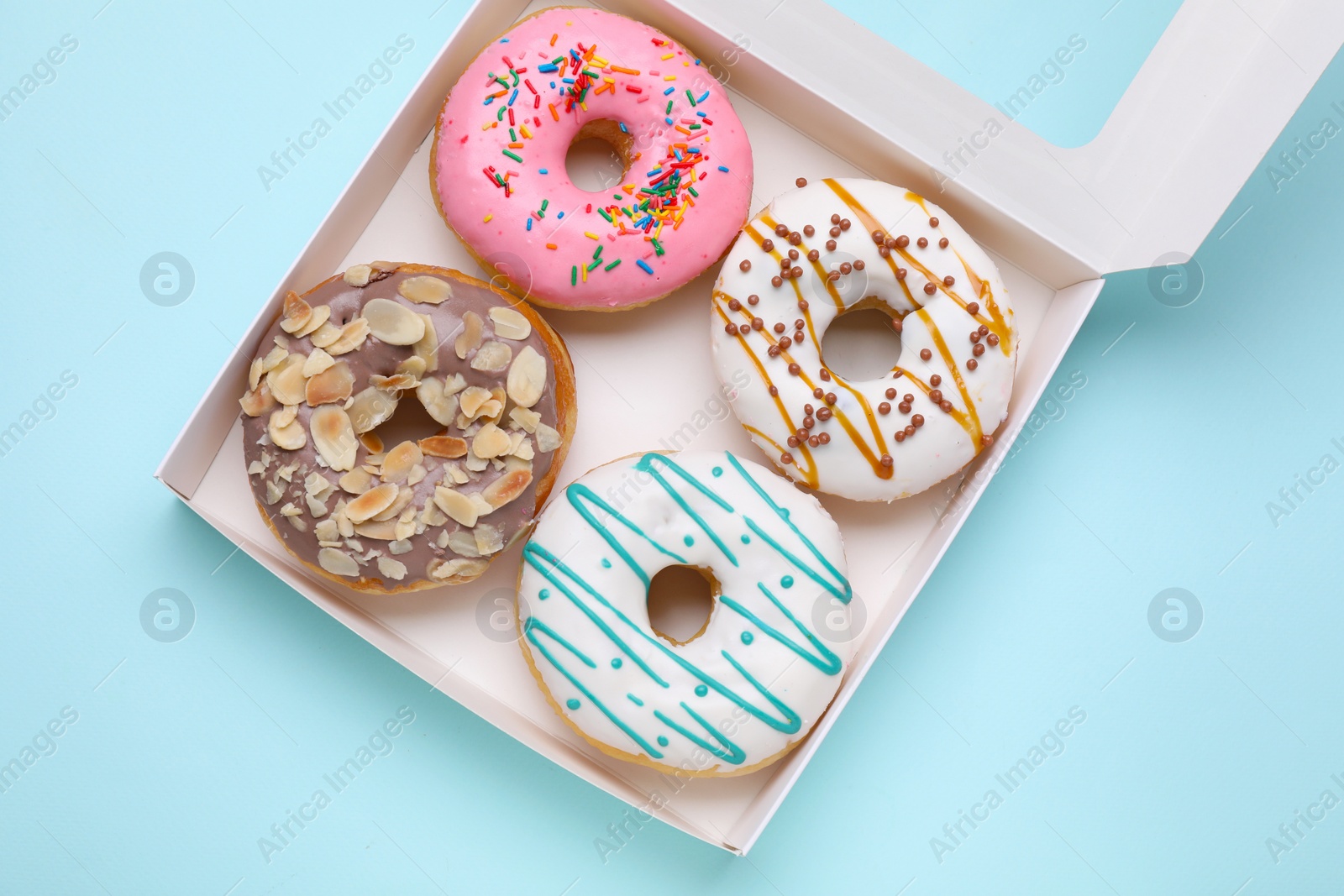 Photo of Box with different tasty glazed donuts on light blue background, top view