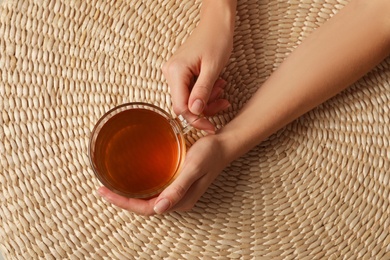 Photo of Woman with cup of black tea at wicker table, top view