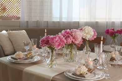 Stylish table setting with beautiful peonies and burning candles indoors