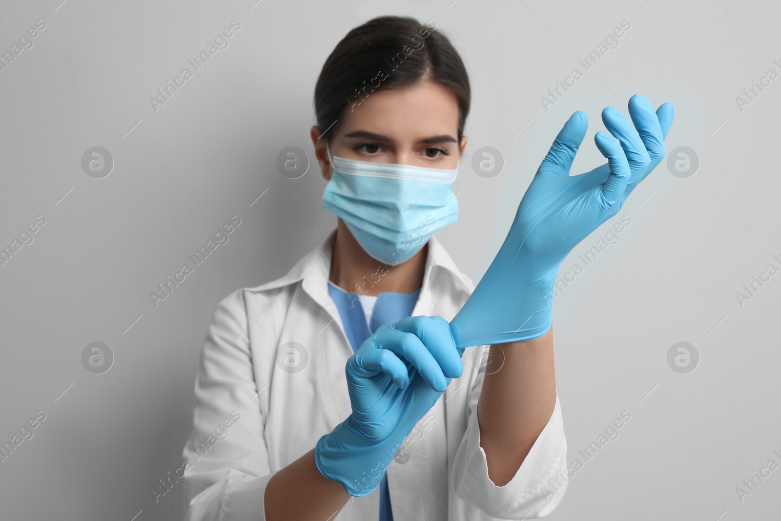 Photo of Doctor in protective mask putting on medical gloves against light grey background