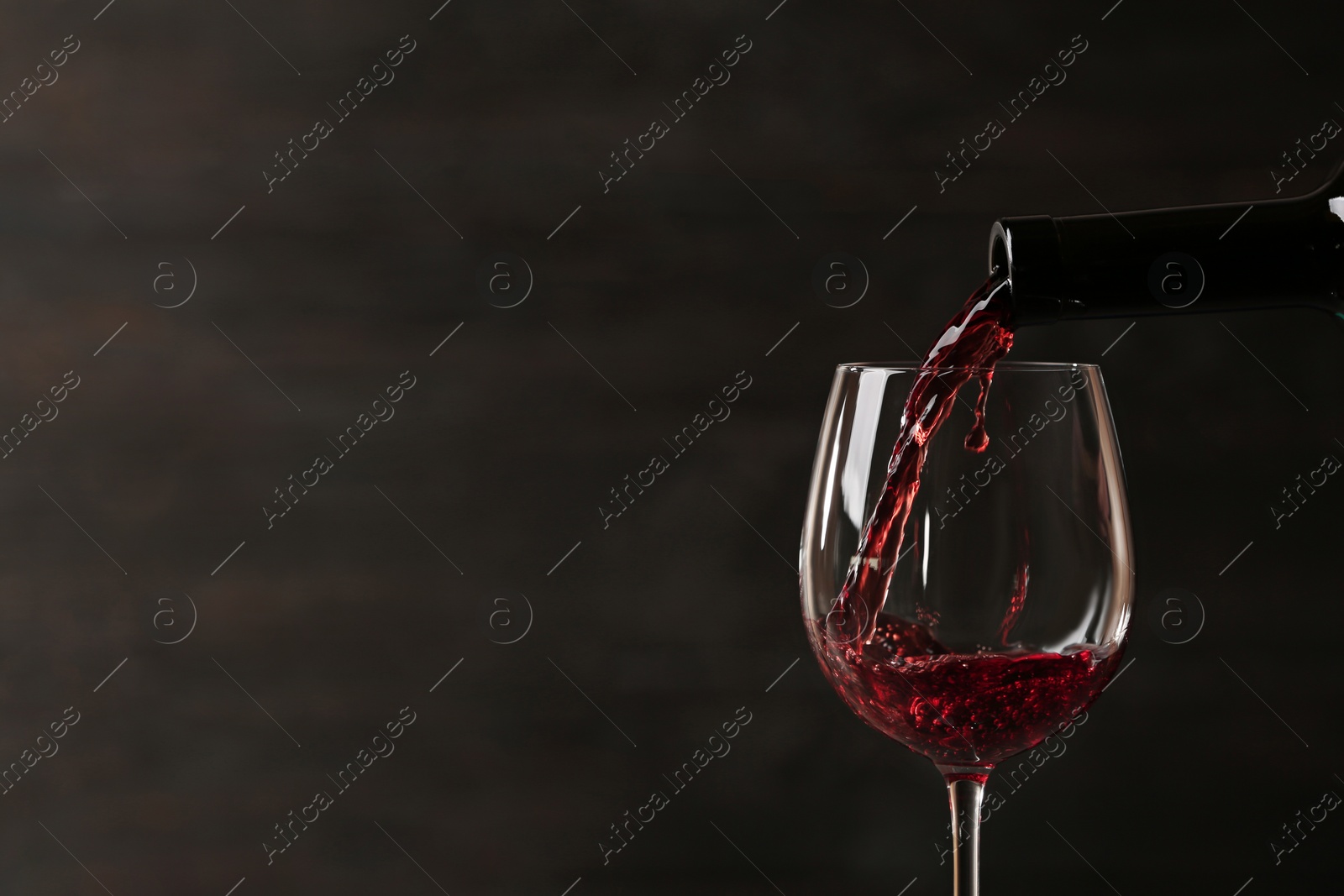 Photo of Pouring red wine into glass from bottle against dark background, closeup. Space for text