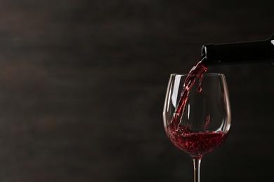 Pouring red wine into glass from bottle against dark background, closeup. Space for text