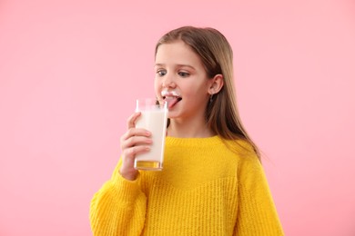 Photo of Funny little girl with milk mustache holding glass of tasty dairy drink on pink background