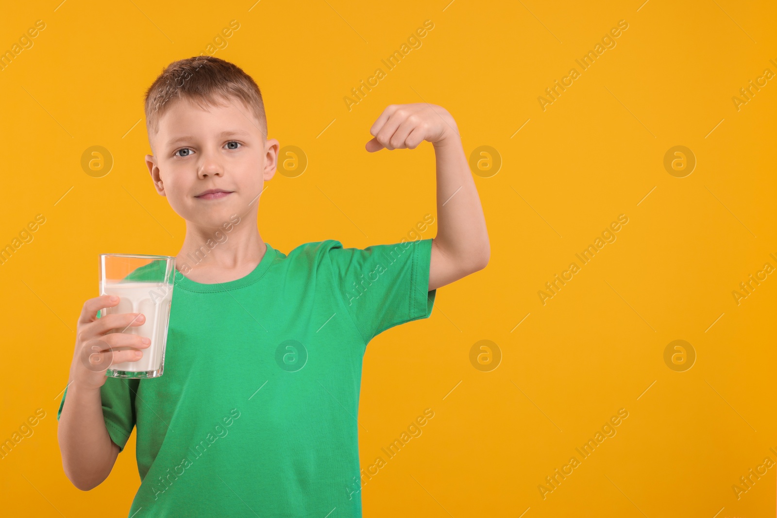 Photo of Cute boy with glass of fresh milk showing his strength on orange background, space for text