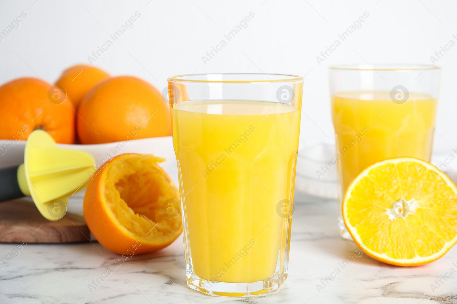 Photo of Fresh ripe oranges, juice and reamer on white marble table