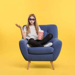 Photo of Emotional teenage girl with 3D glasses and popcorn sitting in armchair during cinema show on color background