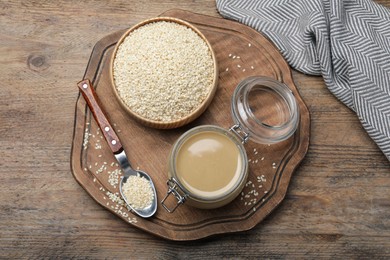 Jar of tasty sesame paste and seeds on wooden table, top view