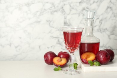 Delicious plum liquor, mint and ripe fruits on white table. Homemade strong alcoholic beverage