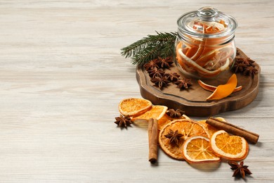 Photo of Dry orange slices, anise stars, cinnamon sticks and fir branches on white wooden table. Space for text