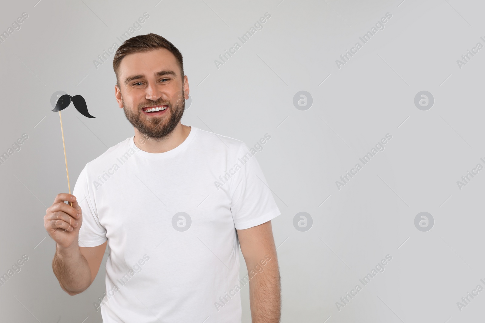 Photo of Funny man with fake mustache on light grey background, space for text