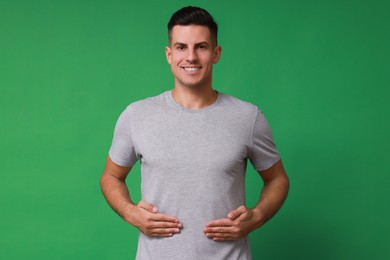 Photo of Handsome man holding hands near stomach on green background