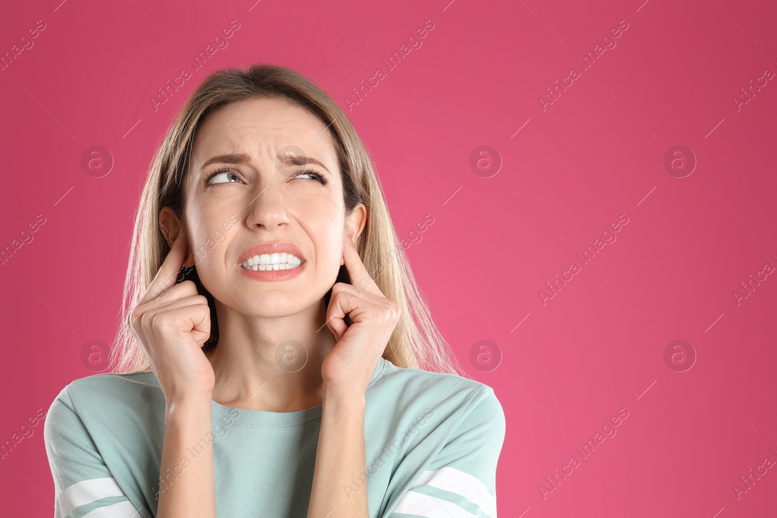 Photo of Emotional young woman covering her ears with fingers on pink background. Space for text