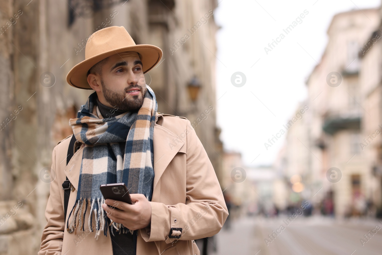 Photo of Handsome man in warm scarf with smartphone outdoors. Space for text